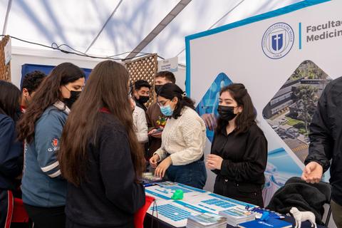 Una feria o evento en el que se observa un stand de la facultad de medicina con varias personas interactuando.