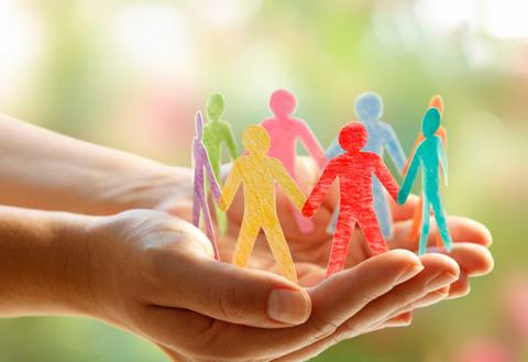 Un par de manos sosteniendo figuras recortadas de personas de colores, simbolizando unidad y apoyo comunitario.