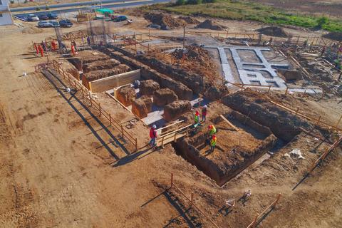Una construcción en proceso con trabajadores y maquinaria en un terreno amplio.