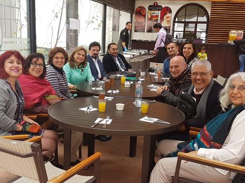 Un grupo de personas se sienta alrededor de una mesa en un restaurante, disfrutando de bebidas y conversando.