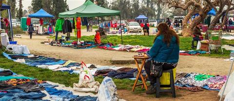 Un mercadillo al aire libre con ropa y gente comprando en un día nublado.