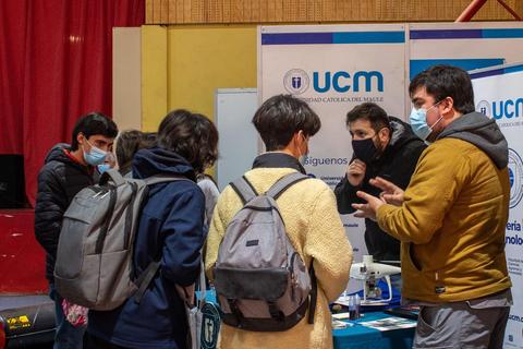 Un grupo de personas jóvenes interactúa en un stand de la Universidad Católica del Murcia durante un evento.