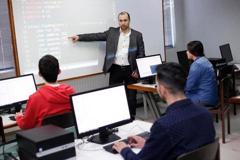 Un profesor está dando una clase sobre programación a un grupo de estudiantes en un aula con computadoras.