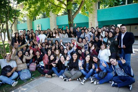Un gran grupo de estudiantes sonrientes se reúne al aire libre para una foto grupal.