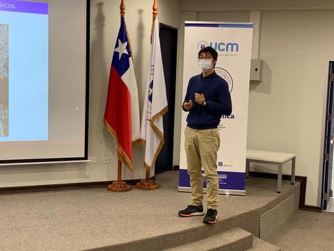 Joven presentando en un auditorio con banderas chilenas de fondo.