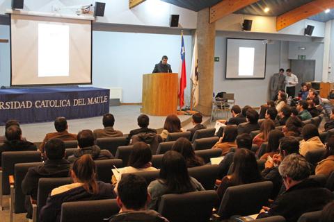 Un conferencista presenta en un auditorio de la Universidad Católica del Maule ante un público atento.