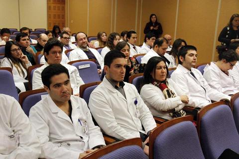 Un grupo de personas en una conferencia, la mayoría vistiendo batas blancas y escuchando atentamente.