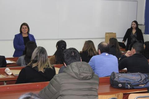 Una mujer está hablando frente a un grupo de personas en un aula.