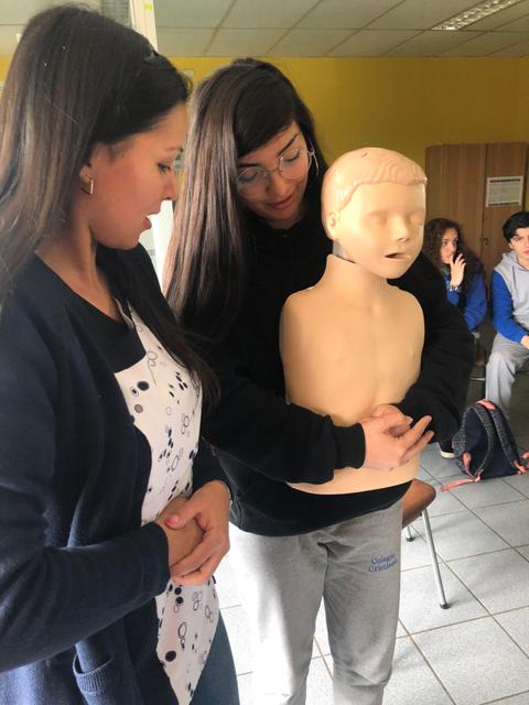 Dos mujeres están practicando técnicas de resucitación con un muñeco en una sala de clases.