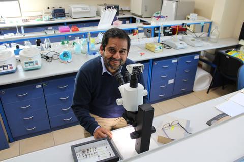 Un científico sonriente trabaja con un microscopio en un laboratorio.