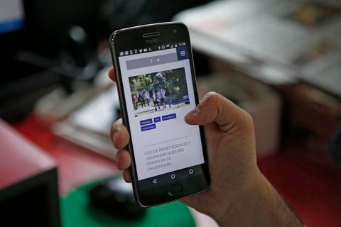 Una persona sostiene un teléfono móvil mostrando una página web con imágenes de varias personas.