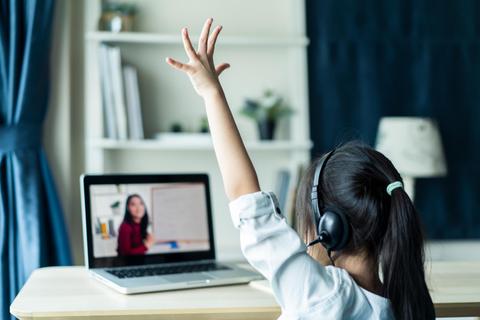 Una niña con auriculares levanta la mano mientras asiste a una clase online en su computadora portátil.