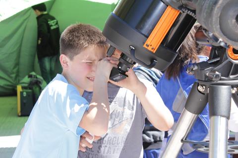 Dos niños observan a través de un telescopio en un evento al aire libre.