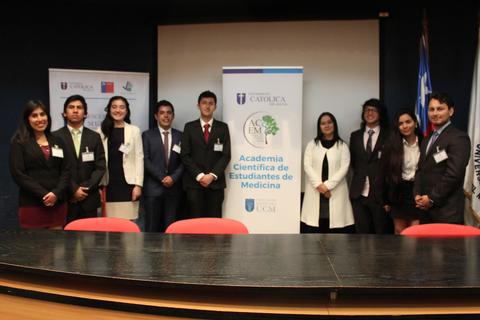 Un grupo de estudiantes de medicina posan frente a un banner de la Academia Científica de Estudiantes de Medicina.