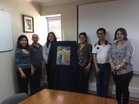 Un grupo de seis personas posan juntas frente a una pintura enmarcada.
