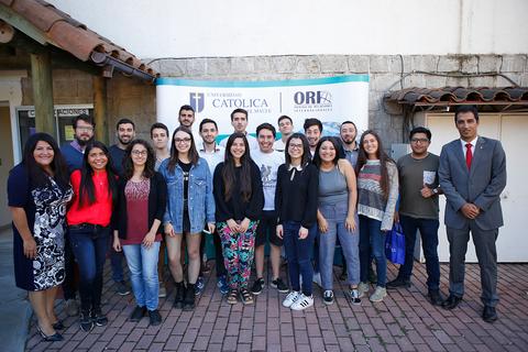 Fotografía grupal de estudiantes frente a un cartel de la Universidad Católica.