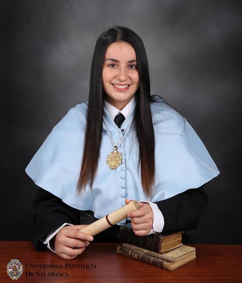 Una graduada sonriente sostiene un diploma y se encuentra vestida con una toga académica.