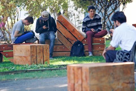 Un grupo de jóvenes sentados en un parque utilizando sus teléfonos móviles.