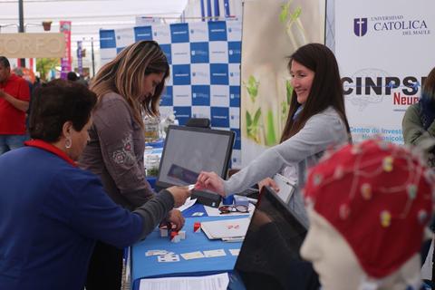 Una interacción en un evento donde dos mujeres conversan y se intercambian información en un stand.