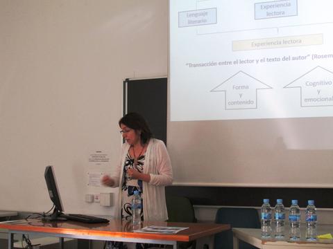 Una mujer está dando una presentación frente a una computadora, acompañada de botellas de agua en una mesa.