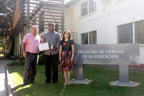 Tres personas posan frente a un edificio de la Facultad de Ciencias de la Educación, sosteniendo un certificado.