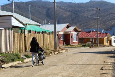 Una mujer camina por una calle de un barrio con casas de colores mientras empuja un cochecito.