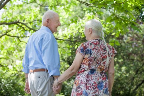 Una pareja de ancianos se toma de la mano mientras pasean por un parque.