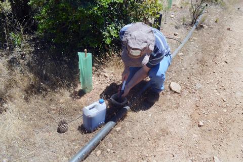 Una persona está trabajando en el suelo junto a una manguera, con un recipiente a su lado.