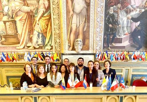 Un grupo de personas posando frente a una mesa decorada con banderas de varios países en un entorno elegante.