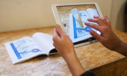 Una persona está utilizando una tableta para interactuar con un libro sobre una mesa.