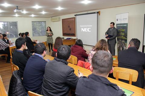 Una presentación en un aula con un expositor frente a un grupo de personas que lo observa.