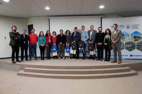 Un grupo de personas posando en un evento en una sala con una presentación detrás.