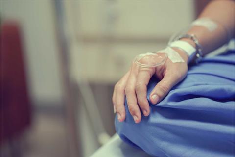 Una mano en un entorno hospitalario que sostiene la ropa de cama mientras recibe atención médica.