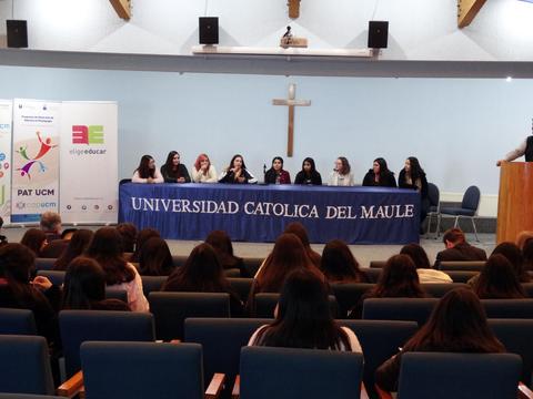Evento en la Universidad Católica del Maule con un panel de mujeres en una mesa frente a una audiencia.