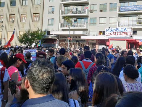 Una multitud de personas se congrega en una manifestación con banderas y carteles en un entorno urbano.