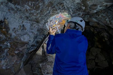 Una persona trabaja en una cueva iluminando una pared con colores brillantes.