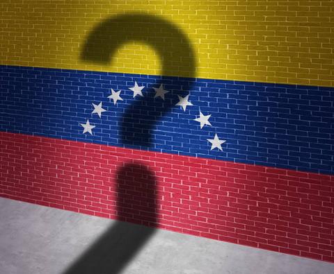 Una pared pintada con la bandera de Venezuela proyecta la sombra de un signo de interrogación.