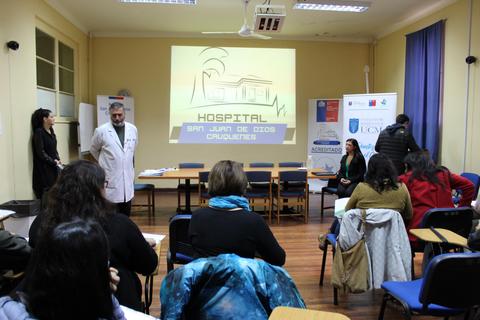 Imagen de una sala de conferencias en un hospital con presentadores y una audiencia sentada.