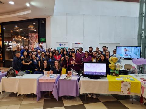Un grupo grande de personas sonríe frente a un stand en un centro comercial.