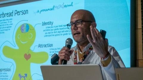 Un presentador masculino expone sobre un tema relacionado con la identidad de género utilizando una ilustración en forma de persona de jengibre.