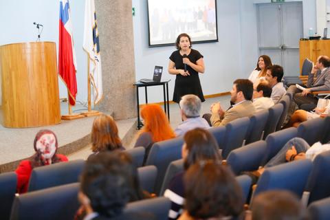 Una mujer está presentando en una conferencia frente a un público sentado en un auditorio.