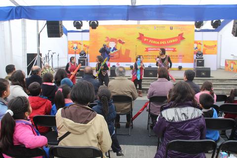 Un grupo de artistas se presenta en un escenario durante la Feria del Libro, mientras el público observa atentamente.