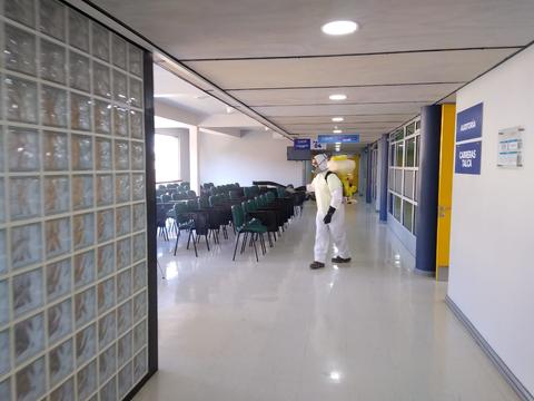 Una persona vestida con un traje de protección camina por un pasillo con sillas vacías.