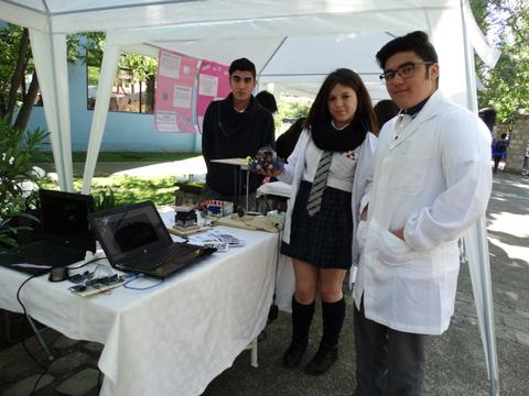 Estudiantes presentan un proyecto en una feria de ciencias con una mesa llena de materiales tecnológicos.