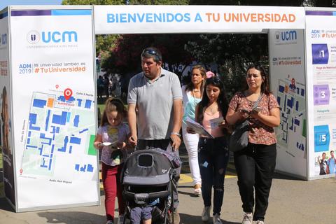 Un grupo de personas camina junto a un cartel de bienvenida a la universidad.