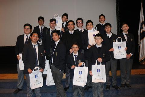 Un grupo de estudiantes vestidos con uniformes escolares posan en un escenario sosteniendo bolsas de eventos.
