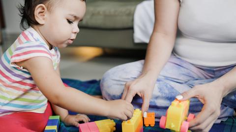 Una niñita juega con bloques de colores junto a su mamá en una alfombra.