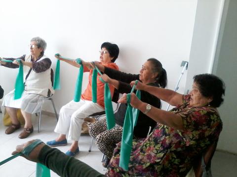 Un grupo de mujeres mayores realizando ejercicios con cintas elásticas en una sala.