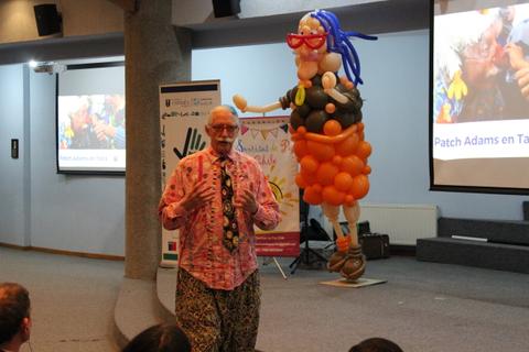 El evento presenta a un orador vestido de manera colorida junto a una figura de globos en forma de mujer.