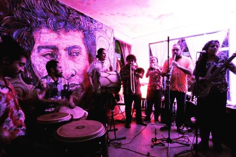 Una banda de músicos toca en un ambiente festivo con un mural de fondo.